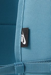 Τεχνητό ύφασμα σε τόνους κυανός, με υφή και σχέδιο, συνοδευόμενο από μια μαύρη ετικέτα Nike και μια υφασμένη ταινία, αναδεικνύοντας μια ανθεκτική σχεδίαση.