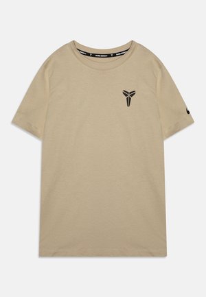 T-shirt beige à manches courtes en coton doux, avec un logo noir sur la poitrine et un swoosh Nike sur la manche, design à col rond.