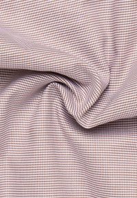 Tessuto intrecciato con un motivo a quadri marrone e bianco, texture liscia e finitura leggermente elastica, disposto in morbide pieghe.