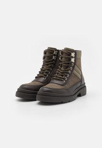 Botas altas de ante y piel texturizada en color verde oliva, con ojetes de metal, suelas gruesas y acentos en los paneles laterales.