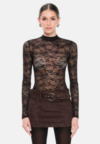 Zwarte kant lange mouwen bodysuit met bloemenpatronen, gecombineerd met een bruin suède minirok met een ronde ceintuur en zakken.