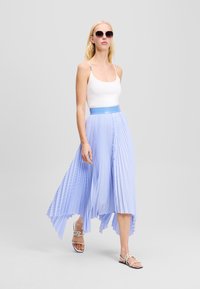 Gonna plissettata azzurro chiaro con orlo asimmetrico, abbinata a una canotta bianca e sandali decorativi, caratterizzata da una texture liscia e una vita elastica.