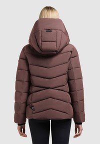 Brown puffer jacket with chevron stitching, a large hood, and a logo tag on the lower left. Soft texture and insulated design.