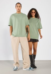 Lysegrønne oversized t-shirts i bomuldsstof, parret med beige bukser og mørke denimshorts, sorte knæhøje støvler og stilfulde briller.
