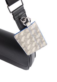 Czarna skórzana torebka z teksturowanym wykończeniem, z beżową etykietą w wzory przymocowaną srebrnym pierścieniem oraz niebieskimi akcentami.