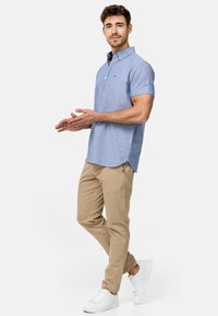 Lys blå kortermet skjorte med knappestolpe og krage, med sidespalter, kombinert med beige bukser og hvite sneakers.