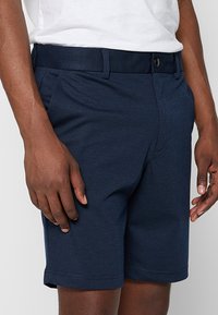 Marineblaue Shorts aus weichem Stoff, mit einem Knopfverschluss, Gürtelschlaufen und Seitentaschen, geradem Schnitt und Saum.