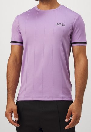 Man wearing a fitted lavender T-shirt with black trim on sleeves and "BOSS" logo on the chest, paired with black pants.