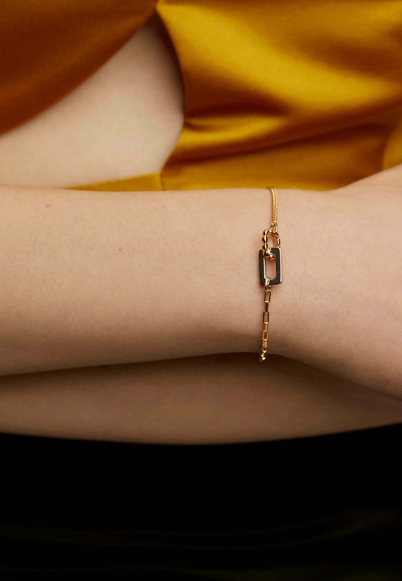 Pulsera de cadena de oro con un acento rectangular en negro y dorado. Diseño elegante con una textura de cadena plana y delicada.