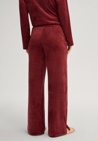 Pantalons lounge bordeaux, doux et veloutés, avec une coupe décontractée, dotés de fentes à l'ourlet et d'une taille élastique pour un maximum de confort.