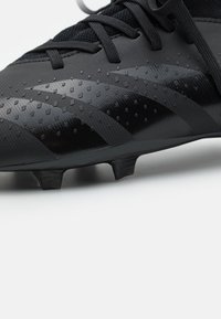 Botín de fútbol negro con un upper texturizado con puntos elevados, área de punta reforzada y múltiples tacos en la suela para tracción.