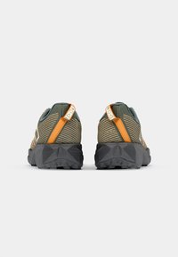 Sneaker a strisce verdi e beige con una grande suola nera testurizzata, linguetta arancione sul tallone e accenti riflettenti.