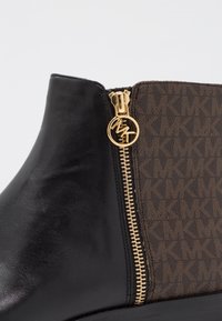 Stivale alla caviglia in pelle nera con stampa monogramma marrone. Presenta una cerniera dorata con tirante con logo e una suola testurizzata.