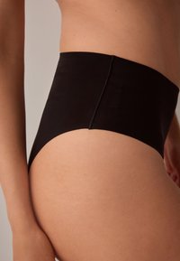 Mutande nere a vita alta realizzate in tessuto liscio, design aderente con finitura senza cuciture e copertura discreta, caratterizzate da un taglio netto.