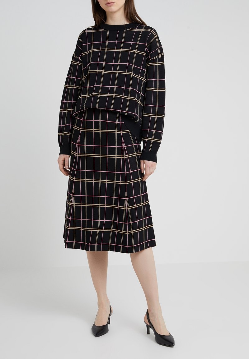 Jersey negro de punto con patrón de cuadros en rosa y dorado, combinado con una falda a juego de cuadros hasta la rodilla. Zapatos negros de tacón completan el conjunto.