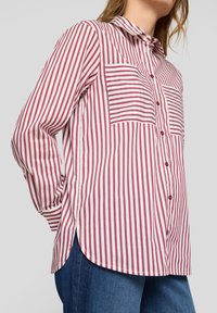 Striped button-up shirt in white and burgundy, featuring two chest pockets, a collar, and a rounded hem. Long sleeves with buttoned cuffs.