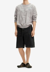 Jasnoszara bluza z fakturowanymi geometrycznymi wzorami, w połączeniu z luźnymi czarnymi szortami jeansowymi i ciemnymi butami wsuwanymi. Prosty design, casualowy krój.