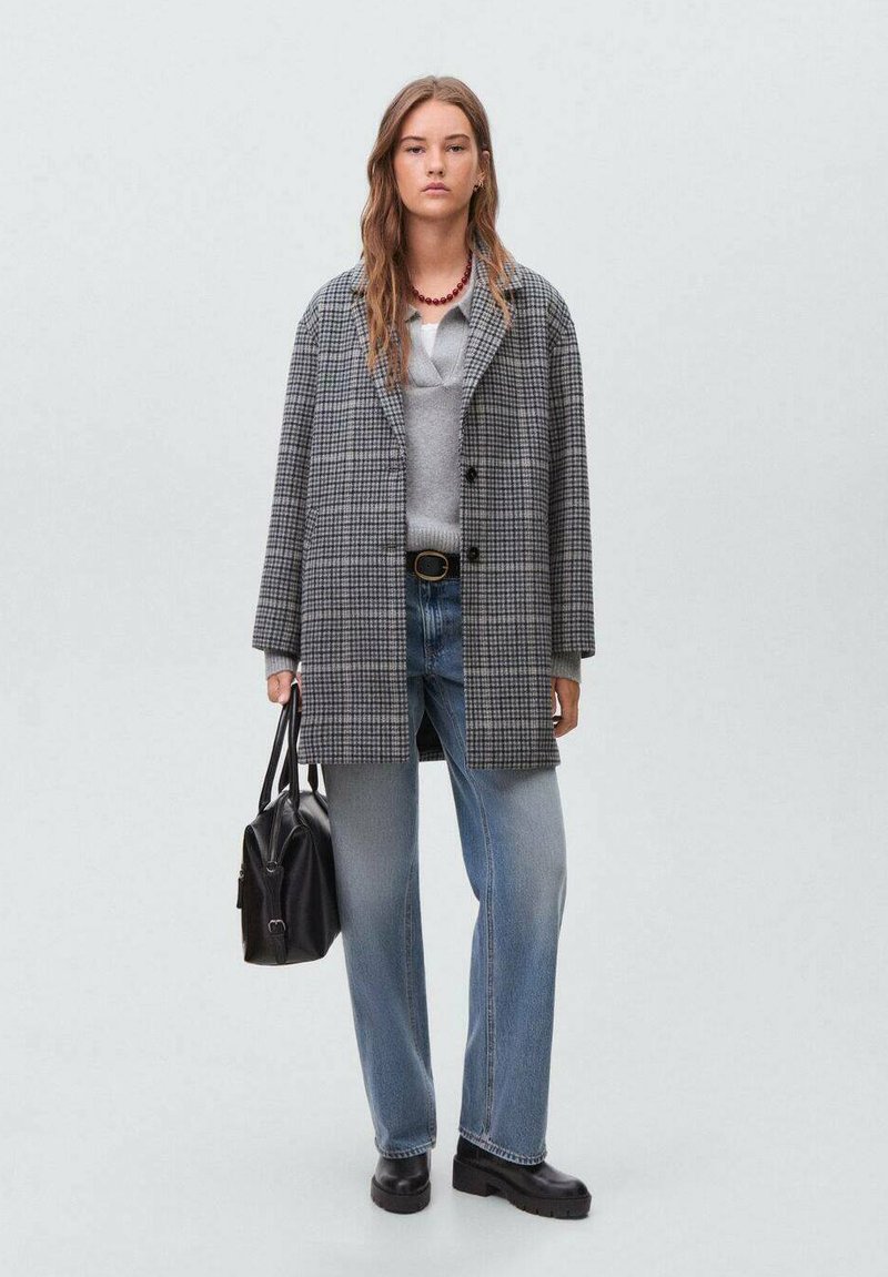 Gray plaid coat with a relaxed fit, paired with a light gray sweater and blue jeans. Black boots and a black handbag complete the outfit.