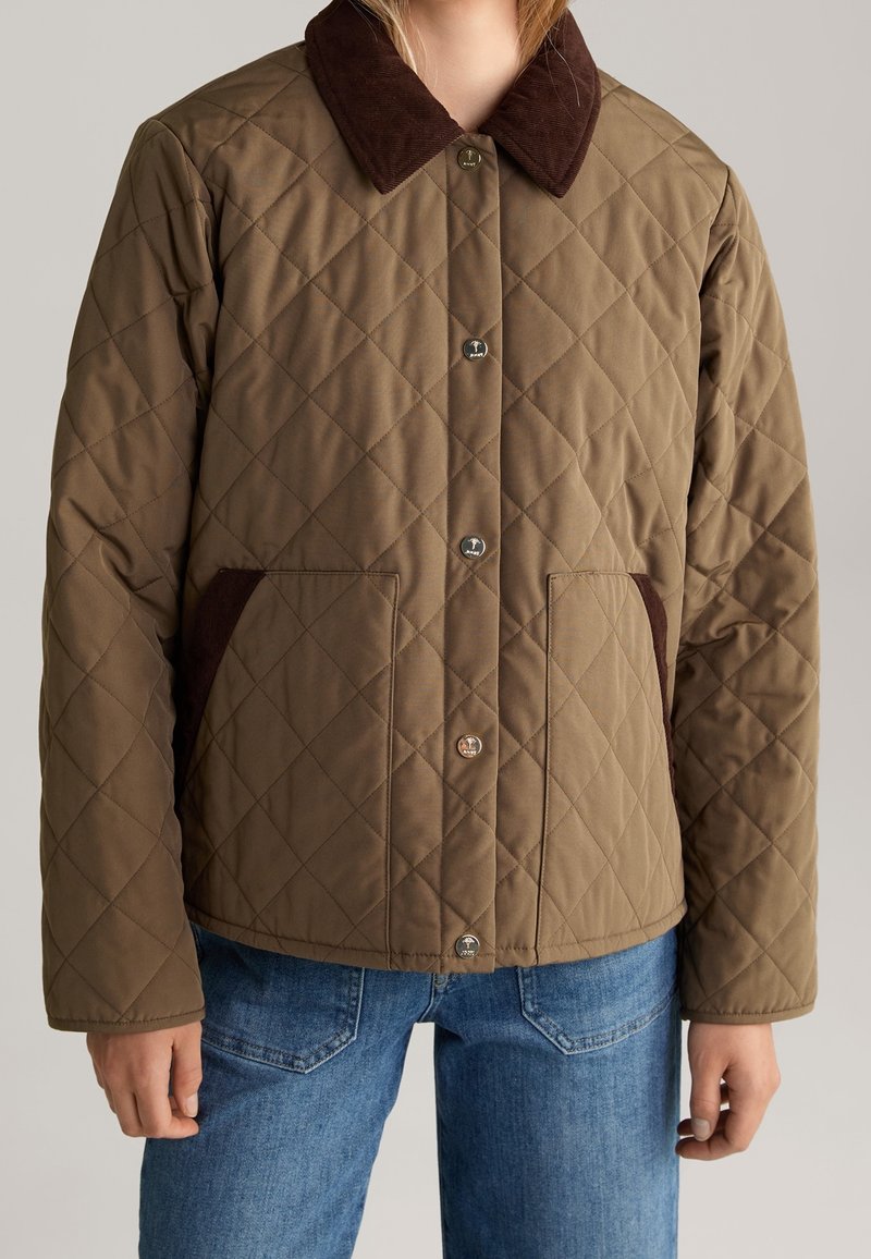 Brown quilted jacket with a corduroy collar, featuring front snap buttons and side pockets, paired with blue denim jeans.