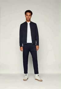 Navy träningsoverall med bomberjacka och avsmalnande byxor. Vit t-shirt under, kombinerad med vita sneakers och en subtil textur.