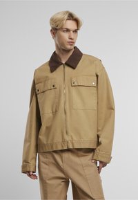 Pruunist korduroost krae, helepruunist puuvillast jakk, millel on lukuga esiosa, kaks rinnataskut ja lõtv istuvus. Sile tekstuur ja tugev õmblus.