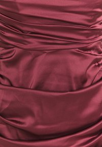 Djupröd tyg med slät satin struktur och draperade veck som skapar mjuka, oregelbundna horisontella rynkor och skuggor.