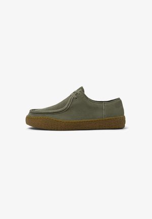 Scarpe in suede verde oliva con punta arrotondata, design a profilo basso e suola in gomma marrone texturizzata. Presentano una scarsa laccatura e dettagli di cucitura minimi.