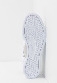 Vit sneaker med en texturerad gummisula, utrustad med en icke-märkande yttersula och Reebok-logotypen präglad på sidan. Mjuk mockadetalj.