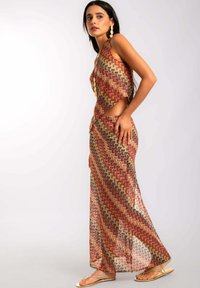 Vestido maxi transparente con patrones geométricos en tonos terrosos. Presenta un corsé ajustado, lados recortados y un dobladillo fluido.