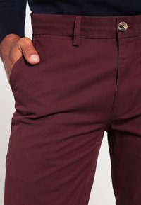 Bordeauxrode katoenen broek met een voorzak, een tonale riemlus en een metalen knoopsluiting met een doorgestikt naaddetail.