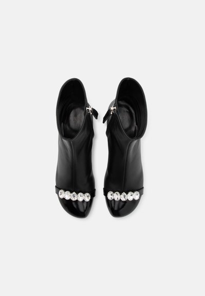 Black open-toed ankle boots made of sleek leather, featuring a shiny band adorned with large clear gemstones and a zip closure at the back.