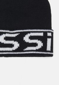 Berretto lavorato a maglia nero con un motivo grafico bianco sul risvolto. Il materiale è morbido, con una trama strutturata.