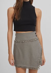 Czarny bezrękawnik w stylu crop top połączony z beżową mini spódnicą w czarne kratki, z frędzlami na dole i bocznymi guzikami.