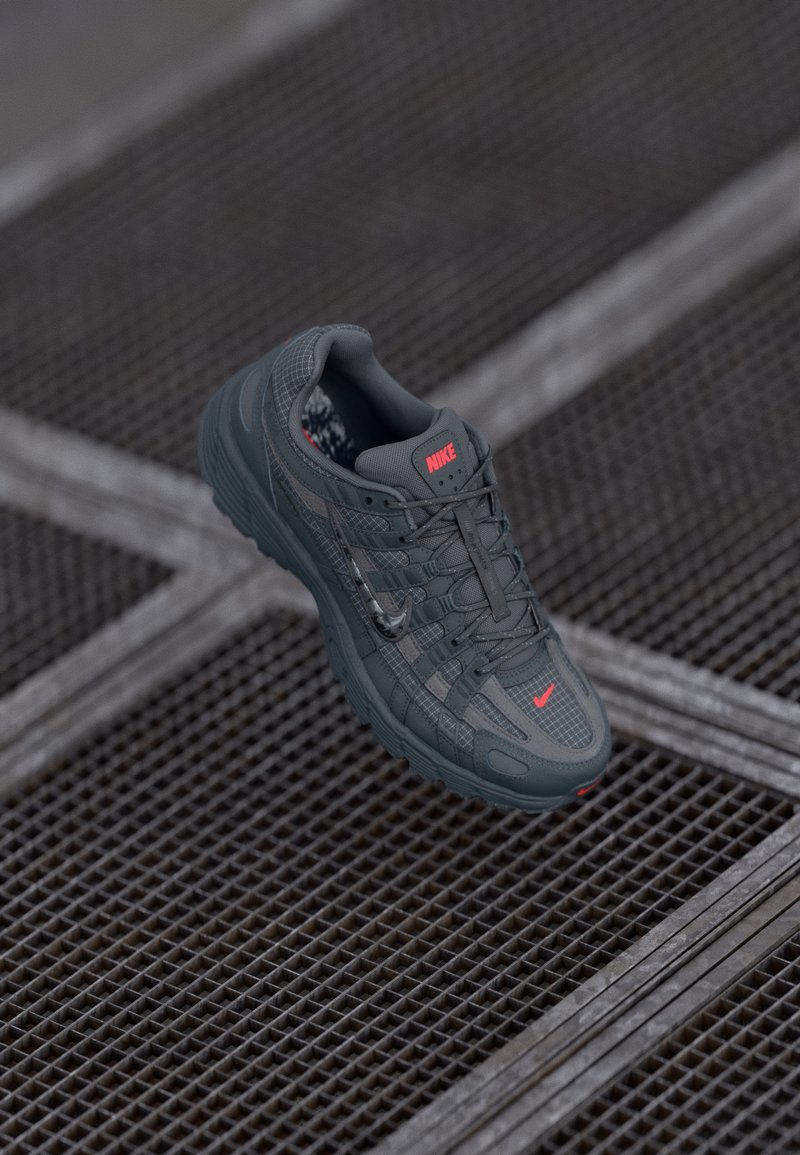 Nike sneakers in dark grey with a textured mesh upper, contrasting red accent logo, and rubber sole, featuring a grid pattern design.