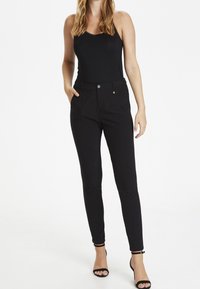 Pantalons slim noirs en tissu extensible, dotés d'une fermeture à bouton, de poches latérales et de subtils accents en métal doré.