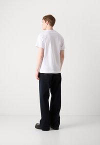 Hvid bomulds t-shirt med korte ærmer, parret med mørkeblå bredbenede bukser. Enkel design, ingen synlige mønstre eller detaljer. Glat tekstur.