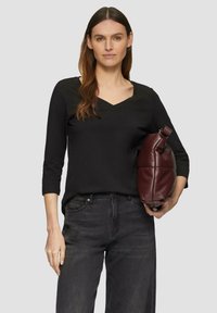 Zwarte V-hals lang mouwen top, gecombineerd met donkergrijze jeans. Houdt een bordeauxrode leren schoudertas vast met een gladde textuur en ronde vorm.