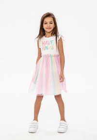 T-shirt blanc avec un texte coloré "HAVE FUN", associé à une jupe en tulle multicolore. Tissu lumineux et léger avec une texture douce.