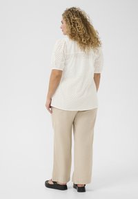 Hvid perforeret bluse med korte pufærmer, parret med beige bredbenede bukser og sorte platform sandaler.