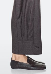 Scarpe slip-on in pelle nera abbinate a pantaloni su misura grigio scuro con dettaglio a bottone e tessuto strutturato.