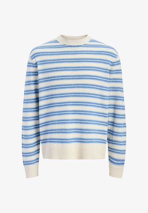 Chłopiec ubrany w niebiesko-biały sweter w paski, jasne jeansowe szorty, białe skarpetki i beżowe buty, stojący i patrzący w prawo na jednolitym tle.