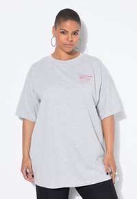 Camiseta gris de gran tamaño hecha de algodón con mangas cortas, que presenta un pequeño logotipo gráfico rosa en la zona del pecho. Cuello redondeado.