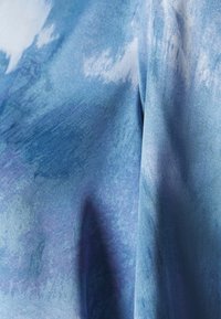 Tissu bleu aux nuances mixtes, présentant une texture lisse et un motif aquarelle dans des tons variés de bleu avec des accents de lavande doux.