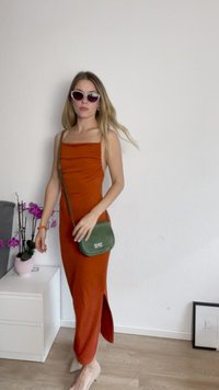 Rūsu krāsas, pieguļošs kleitas modelis ar kvadrātveida dekoltē un sānu izgriezumu; apvienots ar zaļu pleca somu un lielām saulesbrillēm.