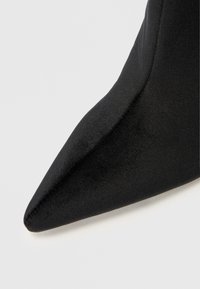 Fekete hegyes orrú magassarkú, sima, szaténszerű textúrával, finom varrással a széleken. Minimalista dizájn, elegáns forma.