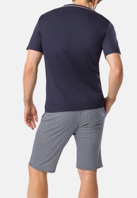 Polo a maniche corte blu navy con rifiniture bianche, abbinato a pantaloni corti a motivi con un design geometrico in tonalità di blu e bianco.