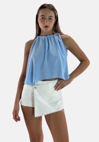 Top halter blu chiaro con scollatura arricciata, abbinato a pantaloni denim bianchi con orlo asimmetrico e bordi sfrangiati.