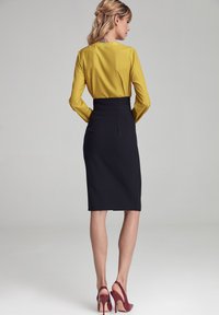 Żółta bluzka z długimi rękawami, zestawiona z czarną ołówkową spódnicą i bordo wysokimi obcasami. Gładka tekstura, dopasowany krój i sylwetka podkreślająca figurę.