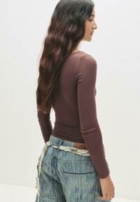 Top fitted a maniche lunghe marrone abbinato a jeans in denim azzurro chiaro con una cintura intrecciata. Il tessuto è morbido, con un design casual.