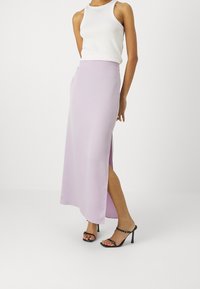 Lila satijnen maxi-rok met een zijsplit, met een soepele textuur en een recht model, gecombineerd met een witte tanktop en zwarte hoge sandalen.